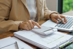Business professional calculating figures on a calculator with financial reports and a laptop