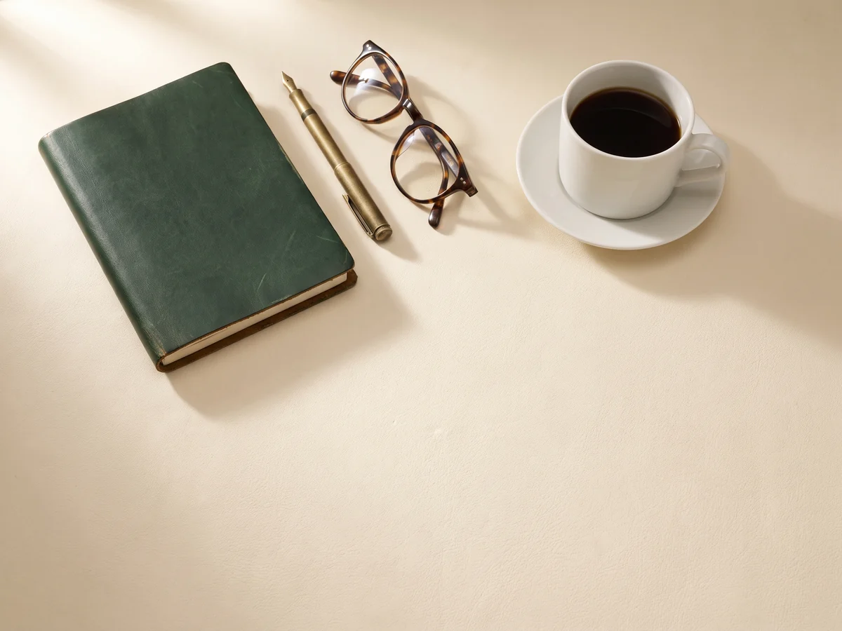 A notebook, pen, reading glasses and a coffee cup on a desk